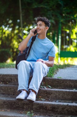 İletişim. Gülümseyen siyah saçlı genç telefonda konuşuyor ve mutlu görünüyor.