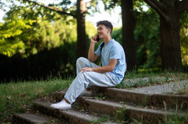 İletişim. Gülümseyen siyah saçlı genç telefonda konuşuyor ve mutlu görünüyor.