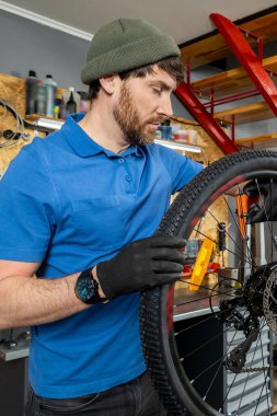 Mavi polo ve bereli genç adam modern atölyede bisiklet tekerleğini tamir ederken odaklanmış görünümü ve siyah eldivenleri olan aletler kullanıyor.