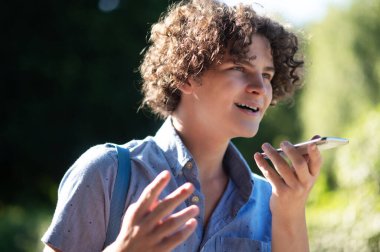 İletişim. Parkta elinde telefon olan kıvırcık saçlı bir genç.
