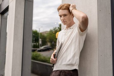 Kızıl saçlı adam dışarıda duvar inşa ederken bilgisayarını kapatmış poz veriyor.