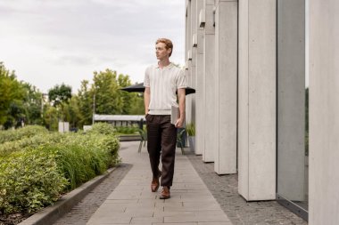 Ofis binasının yakınına taşınan kızıl saçlı adam bina ve yeşillik yolunda yürürken bilgisayarını kapatıyordu.