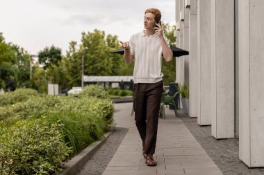 Genç kızıl adam cadde boyunca yürüyordu ve akıllı telefondan konuşuyordu.