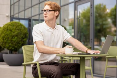 Serbest çalışan adam mesafeyi gözlemliyor seçenekleri değerlendiriyor açık kafede plan yaratıyor