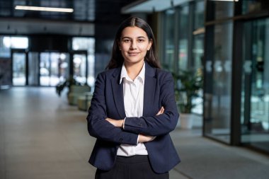 İş merkezindeki genç kadın. Ceketli, beyaz gömlekli, kolları çapraz duran hoş bir genç kadın.