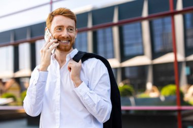 Resmi giyinmiş şık kızıl saçlı şehir merkezinde akıllı telefondan iletişim kuruyor.