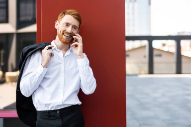 Kızıl saçlı, şık kıyafetli, ceketli ve telefonla konuşan bir adam.