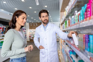 Yeni ürünler. Sakallı beyaz erkek eczacı kadın müşteriye eczanede ilaç gösteriyor.