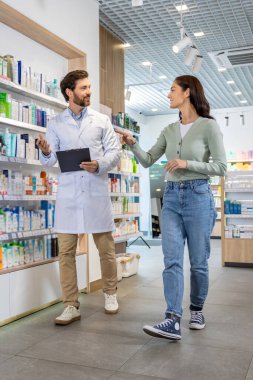 Danışmanlık. Elinde not defteriyle bir kadın müşteriyle konuşan eczane asistanı.