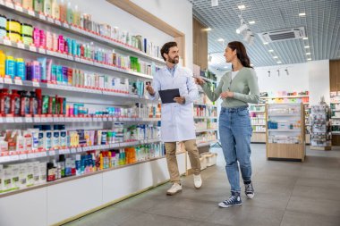 Danışmanlık. Elinde not defteriyle bir kadın müşteriyle konuşan eczane asistanı.