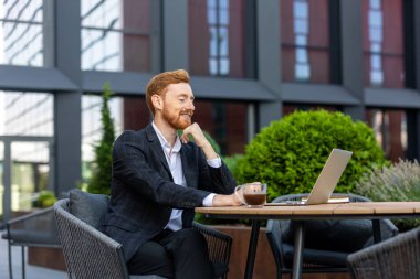Kızıl saçlı iş adamının dışarıdaki kafede bilgisayarında görüntülü arama var.