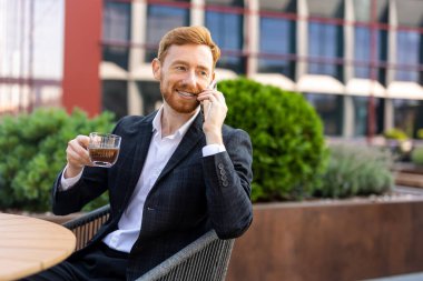 Kafkasyalı profesyonel takım elbiseli, şehirdeki kahve dükkanında telefonda sohbet ediyor.