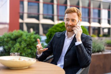 Sakallı işçi, öğle yemeği saatinde kafede cep telefonuyla konuşuyor.