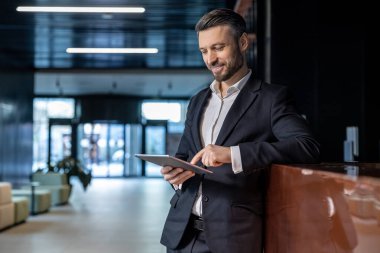 İş yerinde bir adam. Beyaz adam resepsiyonda elinde tabletle duruyor ve kendinden emin görünüyor.