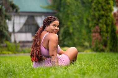 Keyfin yerinde. Genç Afrikalı Amerikalı kadın çimenlerde oturuyor ve kendini harika hissediyor.