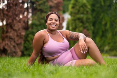 Bahçede dinleniyor. Ayrıca çimde oturan ve sabahtan sonra egzersiz yapan gülümseyen bir genç kadın.