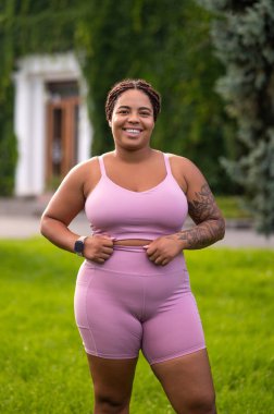 Kendine güven. Pembe spor giysili gülümseyen genç bayan kendinden emin görünüyor.