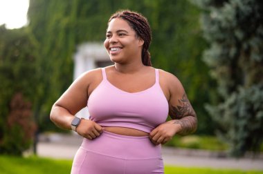 Kendine güven. Pembe spor giysili gülümseyen genç bayan kendinden emin görünüyor.