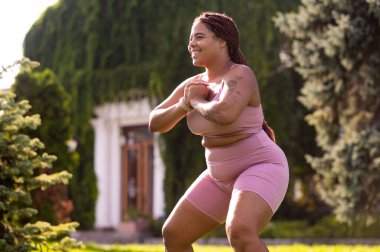 Çömelme. Artı, çimlerde çömelmiş ve kararlı görünen boyda bir kadın.