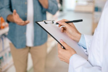 Esmer kadın eczacı, eczanedeki müşteriye danışmanlık yaparken not alıyor.