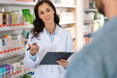Koyu saçlı kadın eczacı, eczanedeki danışmanlık sırasında bilgi kaydediyor.