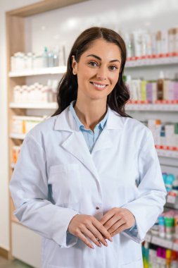 Modern eczane koridorunda dururken gülümseyen beyaz önlüklü kadın eczacı.