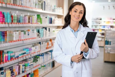 Laboratuvar önlüklü, elinde panoyla gülümseyen eczacı kadın.