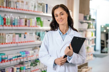Kadın eczacı, Dragstore 'daki ilaç raflarının yanında kendine güvenen bir şekilde duruyor.