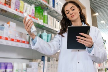 Formalı profesyonel bir kadın elinde bir pano, ilaç malzemelerini kontrol ediyor.