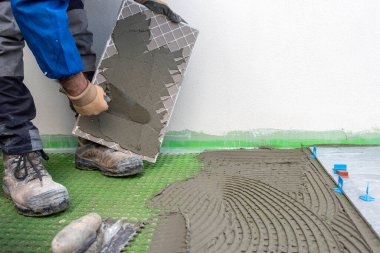 Tuğla ustası tiler yeni zemin fayanslarına malayla yapıştırıcı sürer. İnşaat endüstrisi. İnşa ediliyor.