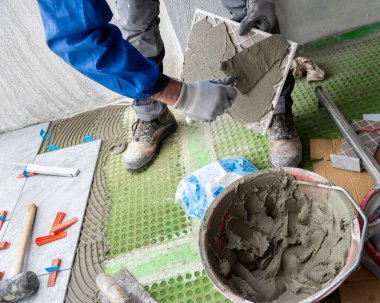 Tuğla ustası tiler yeni zemin fayanslarına malayla yapıştırıcı sürer. İnşaat endüstrisi. İnşa ediliyor.