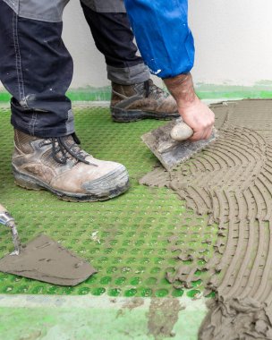 Tuğla ustası tiler, yeni bir zemin için fayansları yerleştirmek için çentik malayla çimento yapıştırıcısı yayar. İnşaat endüstrisi. İnşa ediliyor.