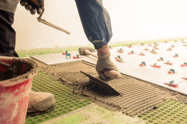 Tuğla ustası tiler, yeni bir zemin için fayansları yerleştirmek için çentik malayla çimento yapıştırıcısı yayar. İnşaat endüstrisi. İnşa ediliyor.