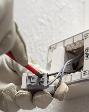 Tornavidayla çalışan elektrik işçisi elektrik sisteminin saptırıcı anahtarının terminallerindeki elektrik kablolarını tamir ediyor. Koruyucu eldivenlerle güvenli bir şekilde çalışmak. İnşaat endüstrisi.