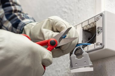 Makasla çalışan elektrik işçisi elektrik sisteminin elektrik kablolarını hazırlıyor. Koruyucu eldivenlerle güvenli bir şekilde çalışmak. İnşaat endüstrisi.
