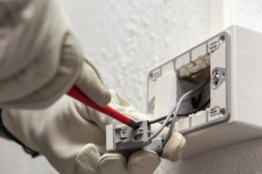 Tornavidayla çalışan elektrik işçisi elektrik sisteminin saptırıcı anahtarının terminallerindeki elektrik kablolarını tamir ediyor. Koruyucu eldivenlerle güvenli bir şekilde çalışmak. İnşaat endüstrisi.