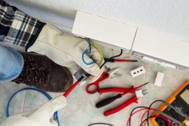 Tornavidayla çalışan elektrik işçisi elektrik sisteminin prizlerindeki elektrik kablolarını tamir ediyor. Koruyucu eldivenlerle güvenli bir şekilde çalışmak. İnşaat endüstrisi.