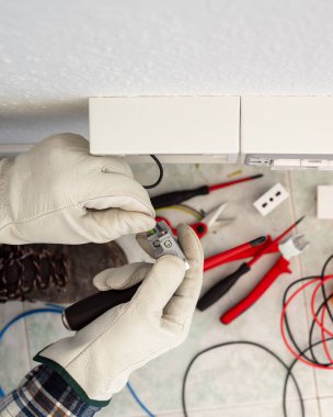 Elektrik işçisi elektrik sisteminin prizlerine elektrik kabloları yerleştiriyor. Koruyucu eldivenlerle güvenli bir şekilde çalışmak. İnşaat endüstrisi.