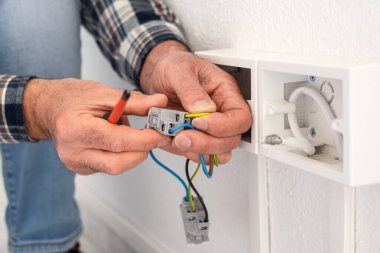 Elektrik işçisi elektrik sisteminin prizlerine elektrik kabloları yerleştiriyor. İnşaat endüstrisi.