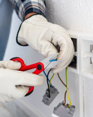 Makasla çalışan elektrik işçisi elektrik sisteminin elektrik kablolarını hazırlıyor. Koruyucu eldivenlerle güvenli bir şekilde çalışmak. İnşaat endüstrisi.