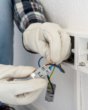 Elektrik işçisi elektrik sisteminin prizlerine elektrik kabloları yerleştiriyor. Koruyucu eldivenlerle güvenli bir şekilde çalışmak. İnşaat endüstrisi.