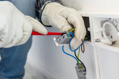 Tornavidayla çalışan elektrik işçisi elektrik sisteminin prizlerindeki elektrik kablolarını tamir ediyor. Koruyucu eldivenlerle güvenli bir şekilde çalışmak. İnşaat endüstrisi.