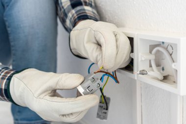 Elektrik işçisi elektrik sisteminin prizlerine elektrik kabloları yerleştiriyor. Koruyucu eldivenlerle güvenli bir şekilde çalışmak. İnşaat endüstrisi.