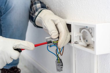 Tornavidayla çalışan elektrik işçisi elektrik sisteminin prizlerindeki elektrik kablolarını tamir ediyor. Koruyucu eldivenlerle güvenli bir şekilde çalışmak. İnşaat endüstrisi.