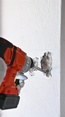 Carpenter electrician with demolition hammer prepares the cavity in the wall where to insert the built-in electrical panel. Work safely with protective gloves. Construction industry. Footage slow motion.