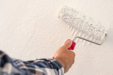 Bir ele yakın çekim. Bir ressam rulo kullanarak duvarları beyaz boyayla boyuyor. İnşaat endüstrisi. 