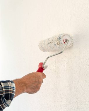 Bir ele yakın çekim. Bir ressam rulo kullanarak duvarları beyaz boyayla boyuyor. İnşaat endüstrisi. 