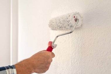 Bir ele yakın çekim. Bir ressam rulo kullanarak duvarları beyaz boyayla boyuyor. İnşaat endüstrisi. 