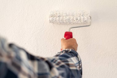 Bir ele yakın çekim. Bir ressam rulo kullanarak duvarları beyaz boyayla boyuyor. İnşaat endüstrisi. 