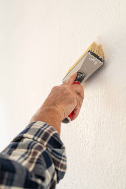 Bir ele yakın çekim. Bir ressam boya fırçasını kullanarak duvarları beyaz boyayla boyar. İnşaat endüstrisi. 